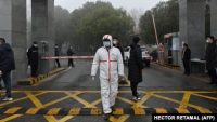 Seorang penjaga mengenakan APD terlihat di pintu masuk pusat pengendalian dan pencegahan penyakit provinsi Hubei saat anggota tim Organisasi Kesehatan Dunia (WHO) meninjau lokasi yang terletak di Wuhan, China, 1 Februari 2021. (Foto: HECTOR RETAMAL / AFP)