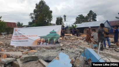 Sekelompok warga berdiri diatas puing-puing bangunan masjid yang roboh akibat gempa di dusun Petakeang, Kecamatan Tapalang, Sulawesi Barat. Jumat (5/1/2021). (Foto: VOA/Yoanes Litha)
