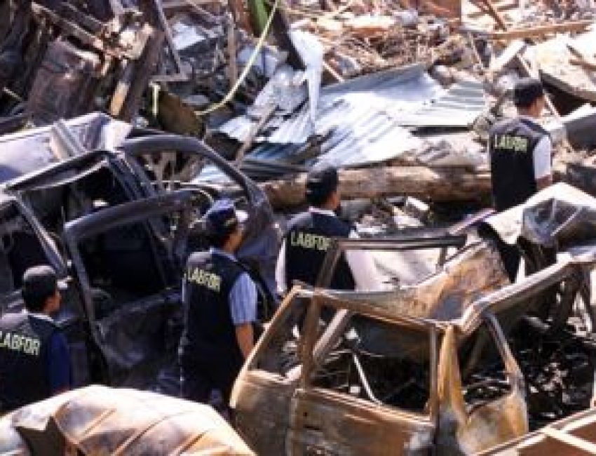 Polisi forensik berjalan melewati mobil-mobil yang hancur di dekat lokasi ledakan bom 12 Oktober 2002 di Kuta, Bali, 18 Oktober 2002. Tiga tersangka yang diduga terlibat pemboman di Indonesia antara tahun 2002-2003 akan diadili pengadilan militer AS. (Foto: Reuters)