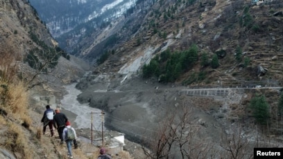 Orang-orang berjalan melewati bendungan yang hancur setelah gletser Himalaya pecah dan menabrak bendungan di Desa Raini Chak Lata di distrik Chamoli, negara bagian utara Uttarakhand, India, 7 Februari 2021. (Foto: Reuters)