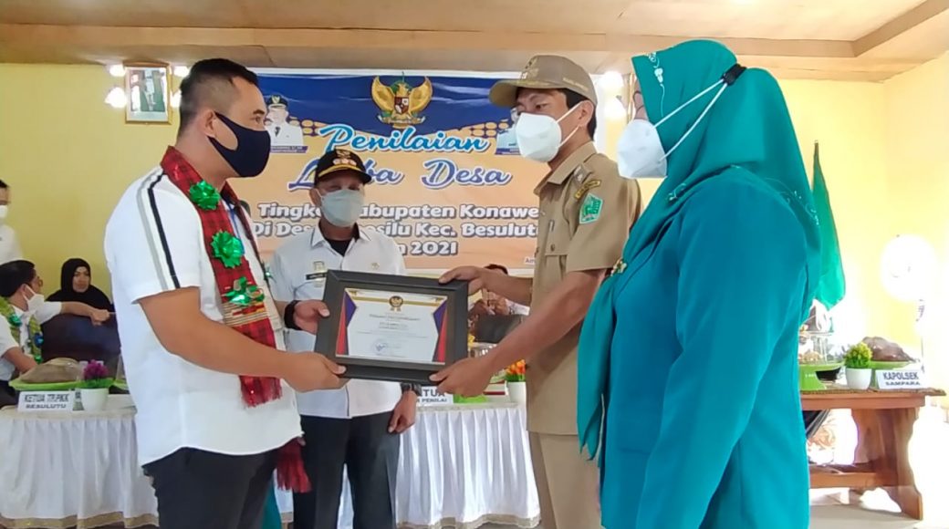 Kepala DPMD Konawe, Keniyuga Permana yang juga ketua Tim Evaluasi saat menyerahkan piagam penghargaan kepada Kades Amosilu Justa, S.sos.