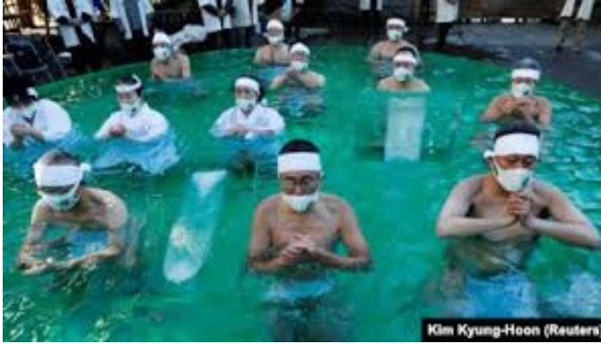 Peserta yang mengenakan masker pelindung wajah di tengah wabah Covid-19, berdoa saat mereka mandi es selama upacara untuk memurnikan jiwa mereka dan berharap untuk mengatasi pandemi di kuil Teppozu Inari di Tokyo, Jepang, 10 Januari 2021. (Foto: REUTERS/K